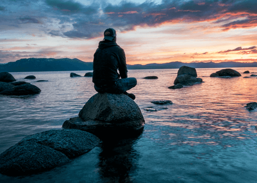 a boy sitting on the rock and watching sunset