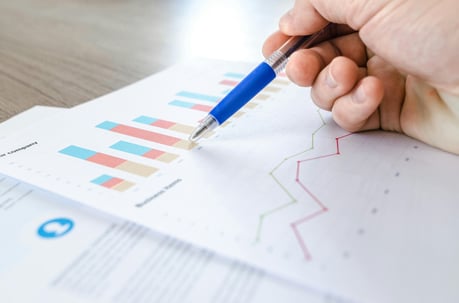 Close-up of a hand holding a pen and pointing at a financial report with bar and line charts.