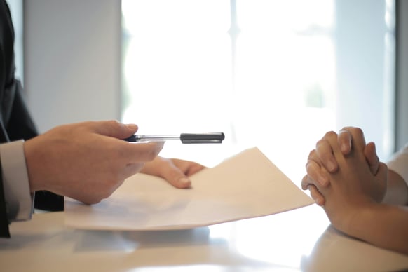 Employer holding a resume and pen while interviewing a candidate at a desk.
