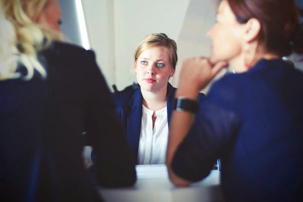 A young professional woman attentively listens during an in-person interview, seated across from two interviewers in a formal setting